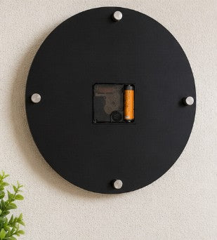 Black circular wall clock with a battery compartment on a light beige wall.