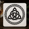 Celtic knot design on a white coaster with a glass of whiskey in the background.