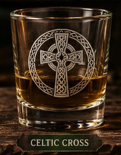 Glass with Celtic cross design filled with a amber liquid on a wooden surface.