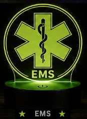 Round EMS LED acrylic night light featuring a glowing green Star of Life emblem mounted on a black LED base, displayed in a dark studio-style setting with illuminated engraved acrylic design.